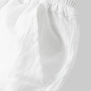 Macro detail shot of white cotton linen pants showing elastic waist and side pocket texture.