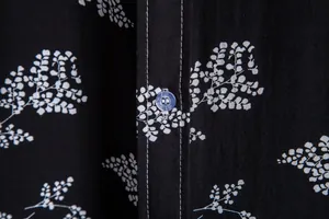 Close-up of black floral shirt fabric with white stitching and blue button detail.