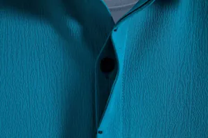 Macro detail of teal textured breathable fabric on men's shirt with black button