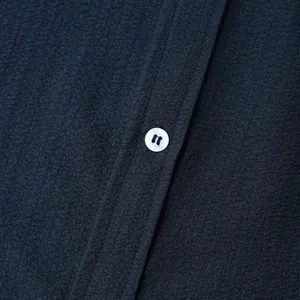 Detailed close-up of navy blue textured fabric and white button on men's short sleeve shirt