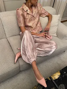 Vista dettagliata di eleganti pantaloni a lanterna in raso rosa con vestibilità ampia e lucida.
