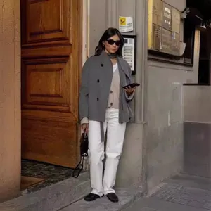 Donna in stile street wear con cappotto di lana grigio doppiopetto e pantaloni bianchi.