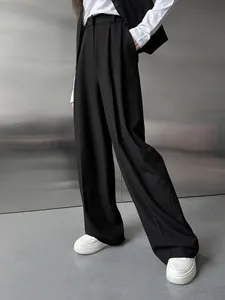 Détail d'un pantalon de costume large noir porté avec des baskets blanches chic