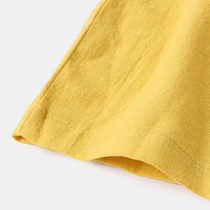 Vue rapprochée montrant l'ourlet piqué et la texture du short jaune en coton et lin