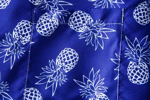 Detailed close-up of white pineapple print on blue tropical Hawaiian short sleeve shirt.