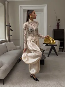 Vista a figura intera di una donna che indossa eleganti pantaloni a lanterna in raso crema.