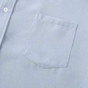 Macro view of light blue textured shirt pocket detailing high-quality fabric and stitching