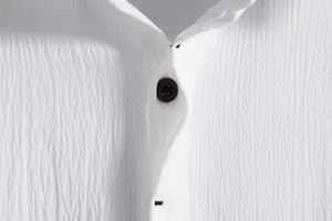 Macro view of white crinkle texture fabric featuring a black button on a men's shirt