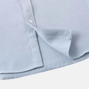 Macro view showing the light blue waffle texture and button detail on men's casual shirt