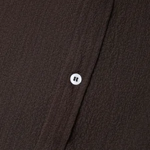 Macro detail showing breathable dark brown fabric texture and white button on a men's shirt