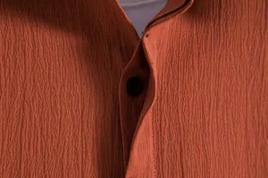 Detailed close-up showing the burnt orange textured fabric and button of a men's shirt