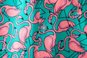 Close-up detail of vibrant pink flamingo pattern on a teal short-sleeve men's shirt