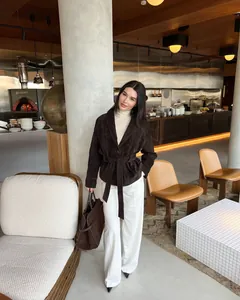 Frau in brauner Vintage-Wildlederjacke mit Gürtel und weißer Hose in modernem Restaurant