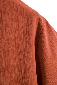 Close-up of the breathable crinkle texture on a men's rust red short-sleeved summer shirt.