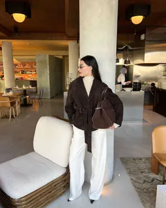 Elegante Frau in dunkelbrauner Retro-Wildlederjacke mit Gürtel in einem Luxus-Café.