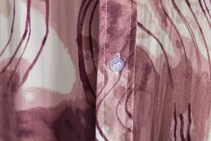 Close-up of men's casual shirt fabric with vintage abstract print and clear button.