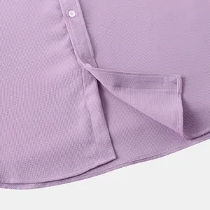 Close-up view of textured purple shirt fabric with white buttons and hemline.