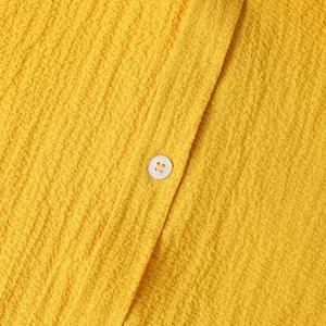 Close-up detail of yellow textured seersucker shirt fabric featuring a white button