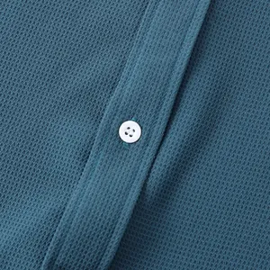 Detailed macro view showing the waffle-knit fabric and white button of a teal casual shirt