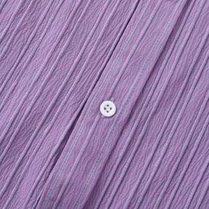 Primer plano detallado de la tela plisada morada y el botón blanco de una camisa de hombre