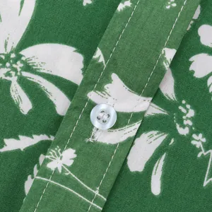 Makroansicht von weißem Blumenmuster und Knopfdetail auf grünem Hawaiihemd