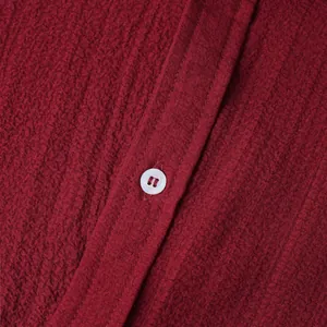 Macro view of dark red textured fabric and white button on a men's casual shirt