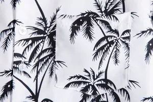 Detalle de camisa blanca para hombre con estampado de palmeras negras y bolsillo.