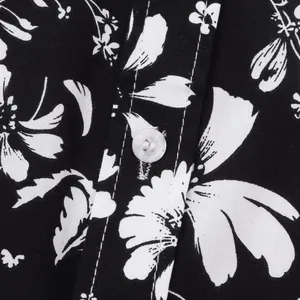 Detailaufnahme eines weißen Knopfes und eleganten Blumenmusters auf schwarzem Hemdenstoff