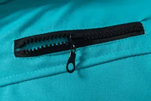 Détail d'une fermeture éclair en résine noire sur un gilet de sport bleu sarcelle