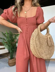 Nahaufnahme eines Terrakotta-Jumpsuits mit Puffärmeln, Smok-Mieder und Strohtasche.