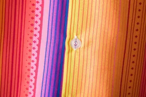 Macro detail of vibrant ethnic striped print and translucent button on Hawaiian shirt fabric