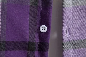 Dettaglio del bottone bianco e della trama del tessuto su una camicia a quadri viola