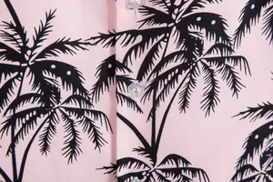 Detalle macro de camisa rosa para hombre con estampado de palmeras negras y botones.