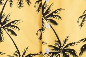 Primer plano del estampado de palmeras negras y botones blancos en camisa amarilla casual