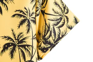 Primer plano del estampado de palmeras negras en tela amarilla de camisa casual de hombre.