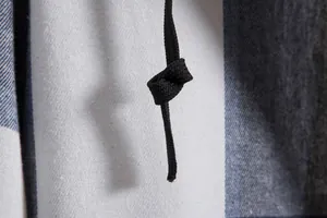Dettaglio macro del cordoncino nero e della trama del tessuto di una camicia a quadri