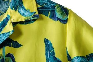 Detail showing the vibrant palm leaf print and collar stitching on a yellow Hawaiian shirt