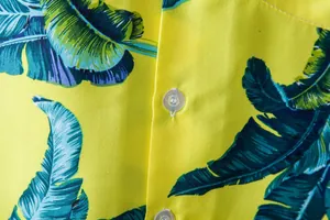Detailed close-up of tropical palm leaf print on yellow men's Hawaiian short shirt
