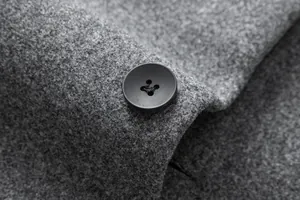 Close-up of a premium grey wool blend fabric and black button on a men's winter overcoat.