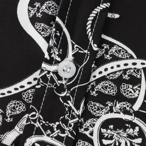 Dettaglio ravvicinato di una camicia con stampa paisley bianca e nera, bottone e cuciture.