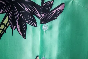 Macro detail of green Hawaiian shirt fabric featuring a tropical palm leaf print and button.
