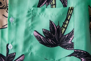 Macro detail of pocket stitching and tropical palm tree print on men's green Hawaiian shirt