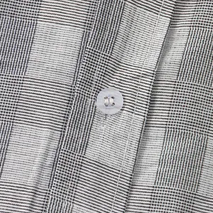 Dettaglio ravvicinato di camicia a quadri grigia da uomo con bottone e cuciture.