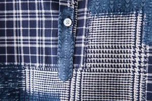 Macro detail of blue patchwork shirt with white button placket texture.