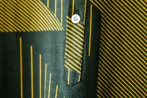 Macro detail of men's cotton-linen shirt with yellow geometric lines and white button.