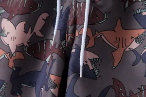 Macro detail of men's swimming trunks with colorful shark print and white drawstring.