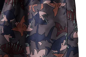 Close-up of durable fabric on men's beach shorts with colorful shark pattern.