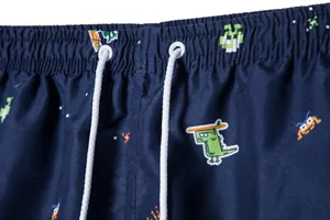 Close-up detail of men's navy blue beach shorts with cartoon dinosaur and pixel print