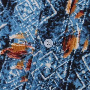 Makroansicht von blauem Ethno-Blumenmuster und Knopf an einem lässigen Herren-Strandhemd