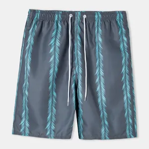 Detail of men's beach shorts featuring vertical teal leaf patterns and white drawstrings
